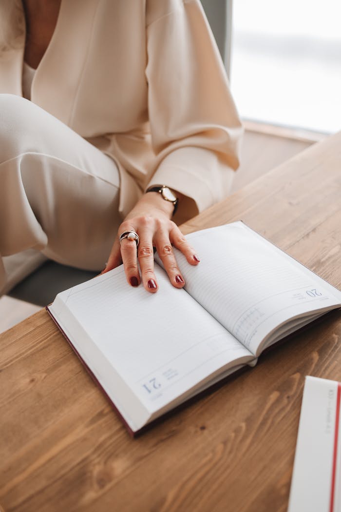 Close-up of a woman's hand on an open diary on a wooden table, capturing an intimate reading moment indoors.